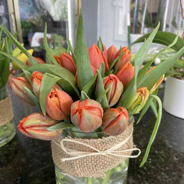 Orange tulip bouquet in a glass vase wrapped with burlap and ribbon
