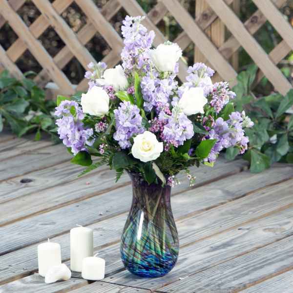 Lavender and white flowers arranged in a glass vase beside white candles
