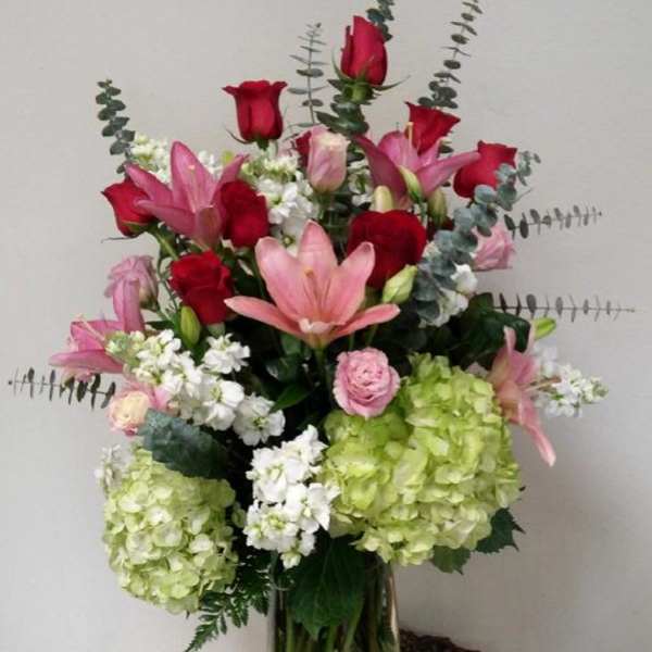 Tall bouquet of red roses, pink lilies, and green hydrangeas in a glass vase