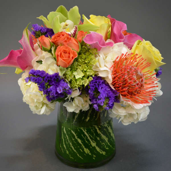 Colorful bouquet with roses, calla lilies, and a protea in a glass vase