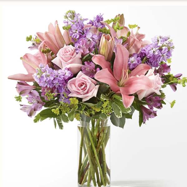 Pink roses and lilies with purple flowers in a clear glass vase