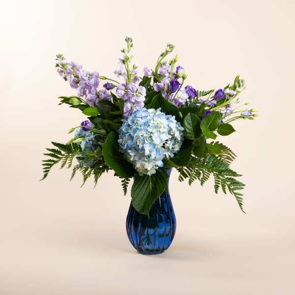 Blue hydrangeas and purple flowers in a blue glass vase