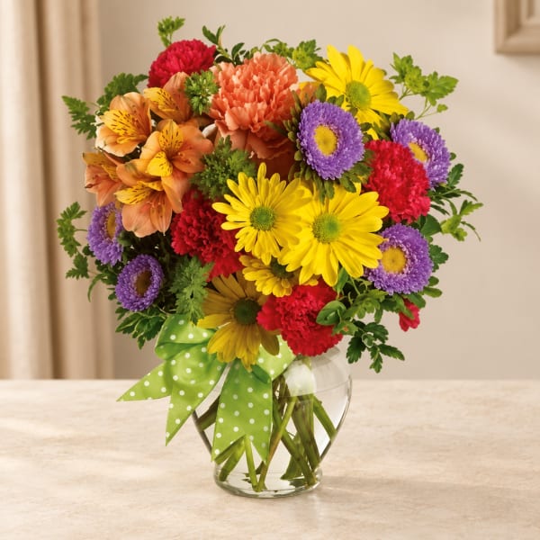 Colorful mixed bouquet in a clear glass vase with a green polka-dot ribbon