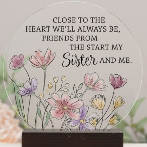 Round memorial plaque with floral illustration and sister quote on a wooden stand
