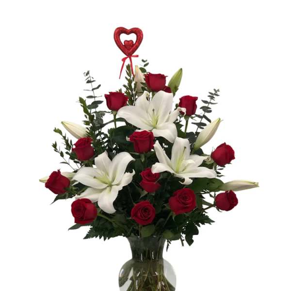 Red roses and white lilies in a clear glass vase with a heart pick