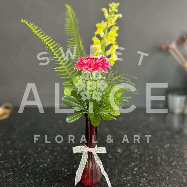 Pink and yellow flowers in a small red vase with a ribbon