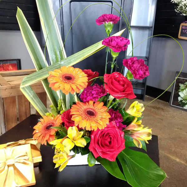 Bright mixed bouquet with roses, gerbera daisies, carnations, and alstroemeria in a white container