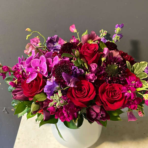 Bouquet of red roses and purple flowers in a white vase