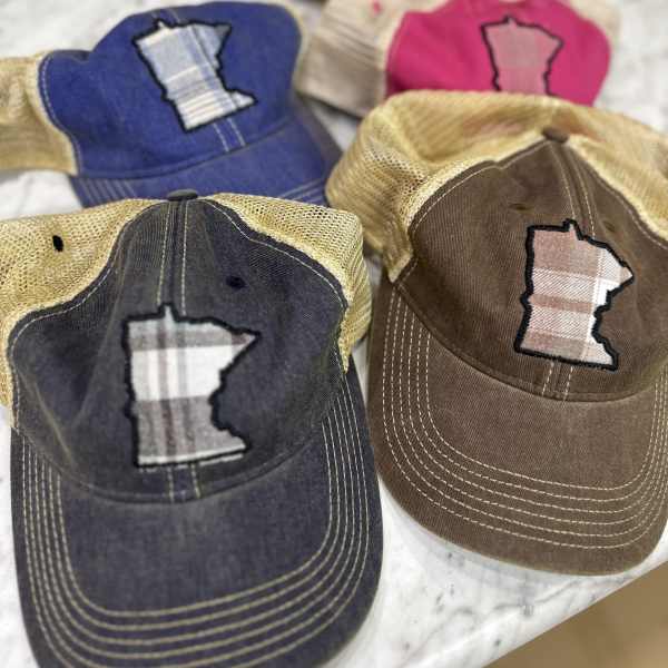 Four baseball caps with Minnesota-shaped patches arranged on a light surface.