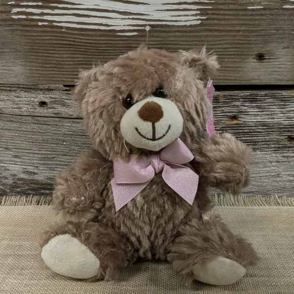 Brown teddy bear with a pink bow sitting on burlap