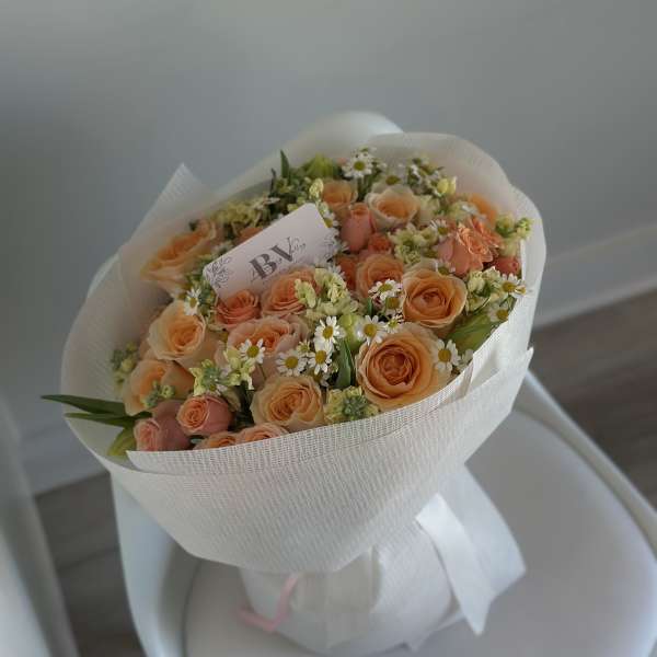 Peach rose bouquet with small white daisies wrapped in white paper