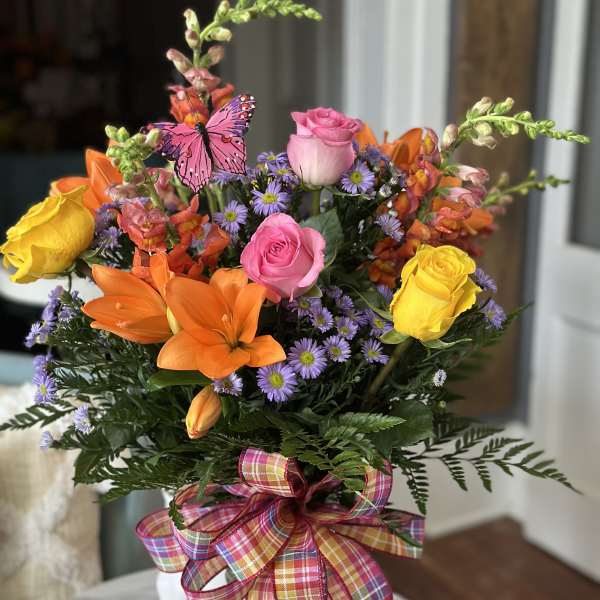 Colorful bouquet of roses, lilies, and purple daisies in a glass vase with a plaid ribbon.