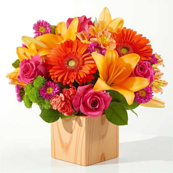 Bright mixed bouquet in a wooden cube vase with roses and lilies