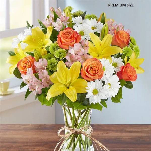 Bouquet of yellow lilies, orange roses, and white daisies in a glass vase