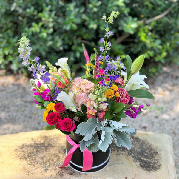 Colorful mixed flower arrangement in a black hatbox with a pink ribbon
