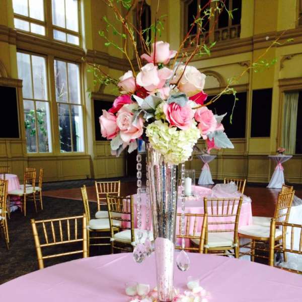 Tall pink and white floral centerpiece in a mirrored vase on a pink tablecloth