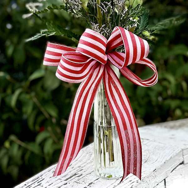 Single red rose in a clear glass vase with a striped ribbon bow
