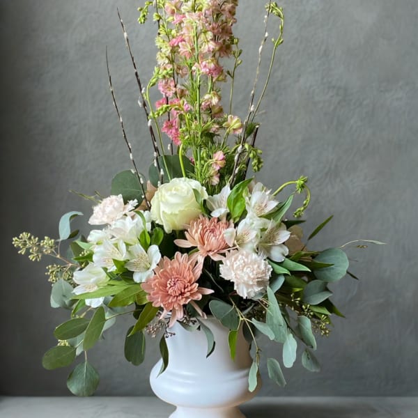 Pastel floral arrangement in a white pedestal vase with tall pink blooms