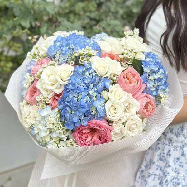 Large bouquet of blue hydrangeas and pink and white roses wrapped in pale paper