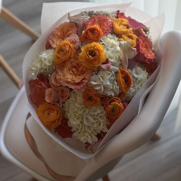 Bouquet of orange and peach flowers with white hydrangeas in pink wrap