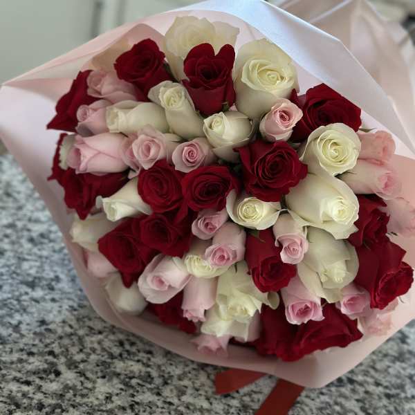 Bouquet of red, white, and pink roses wrapped in pale pink paper