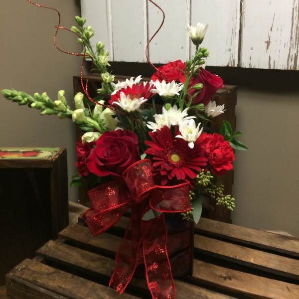 Red and white mixed flower arrangement in a dark vase with a red ribbon