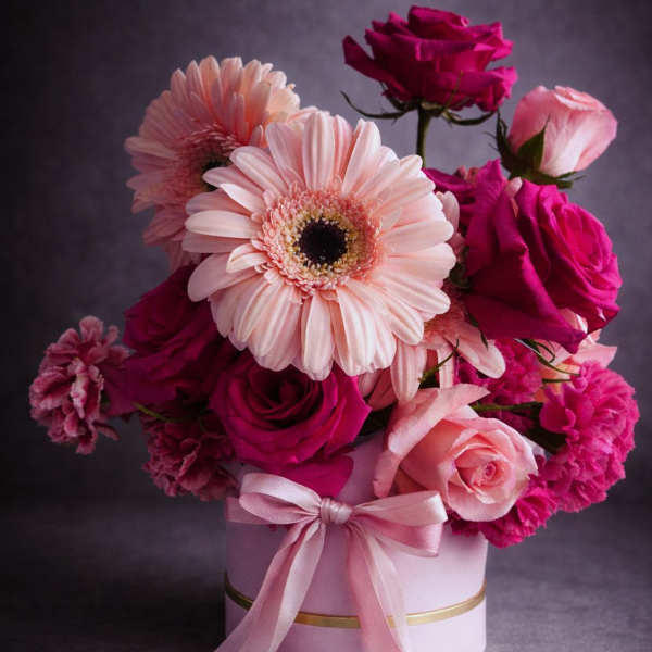 Pink and magenta flower arrangement in a round box with a ribbon