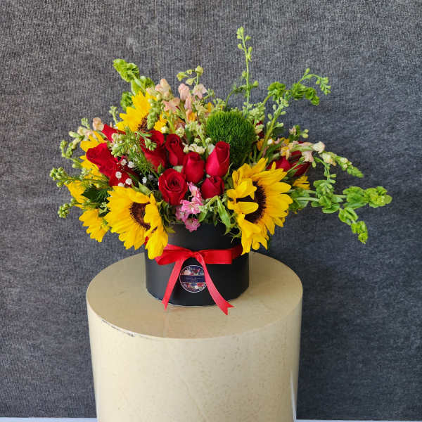 Bouquet of red roses and yellow sunflowers in a black box with a red ribbon