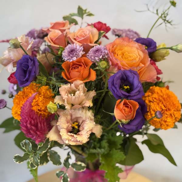 Mixed bouquet of orange, purple, and pink flowers in a glass vase