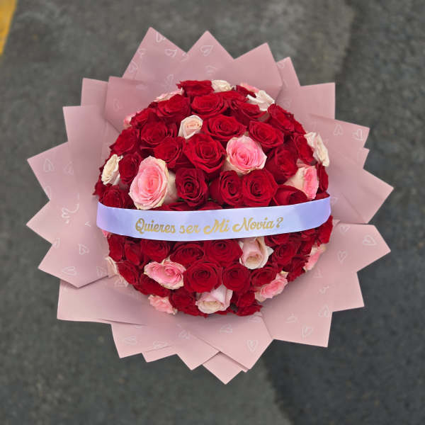 Round bouquet of red and pink roses wrapped in pink paper with a ribbon