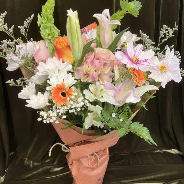 Mixed bouquet of lilies, roses, daisies, and orange gerbera daisies wrapped in pink paper