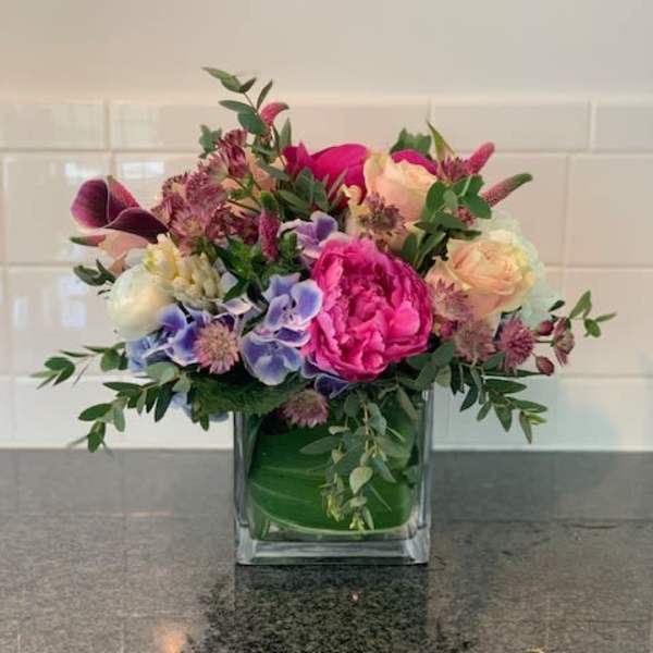 Mixed bouquet in a square glass vase with pink, peach, purple, and white blooms