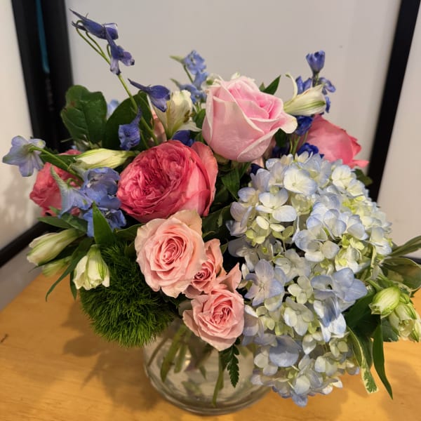 Mixed bouquet of pink roses, blue hydrangea, and blue flowers in a glass vase
