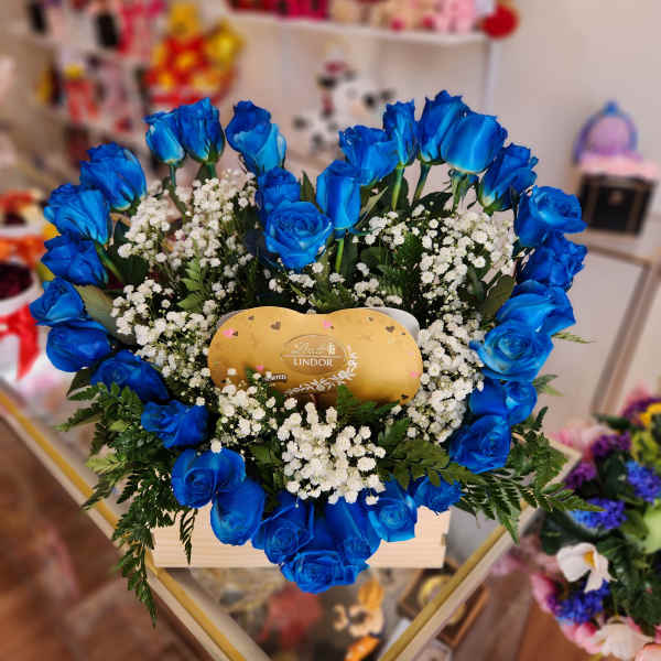 Blue roses arranged around a gold Lindor chocolate box