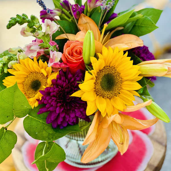 Bouquet with sunflowers, roses, and orange lilies in a glass vase
