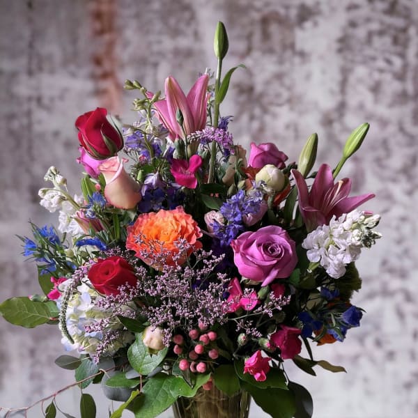 Mixed bouquet of roses, lilies, and purple flowers in a glass vase