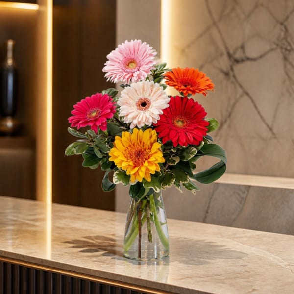 Colorful gerbera daisy bouquet in a clear glass vase on a countertop