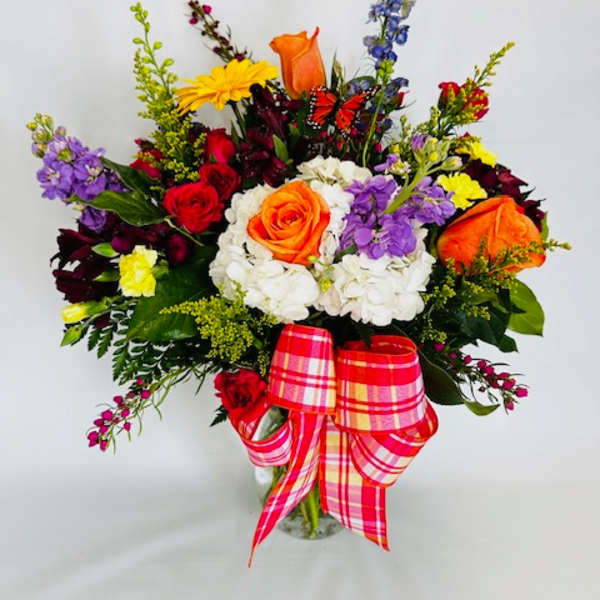 Colorful mixed flower bouquet in a glass vase with a plaid ribbon
