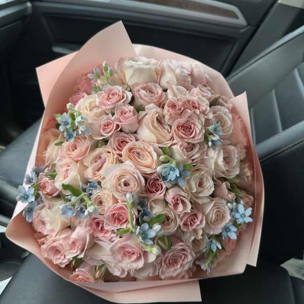 Bouquet of pale pink roses with small blue flowers wrapped in pink paper