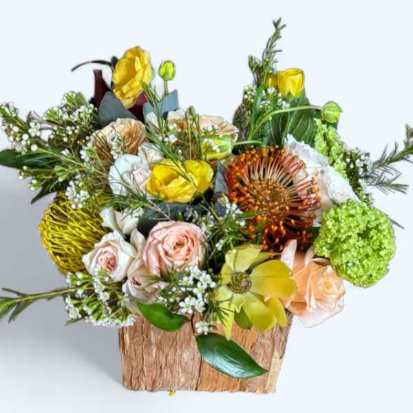 Mixed bouquet in a rustic wooden container with yellow, peach, white, and green blooms