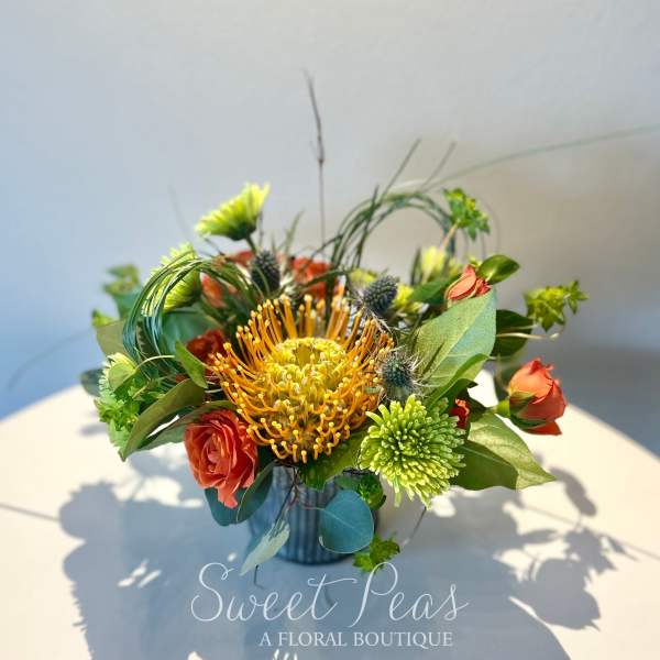Orange pincushion protea with red roses in a small vase