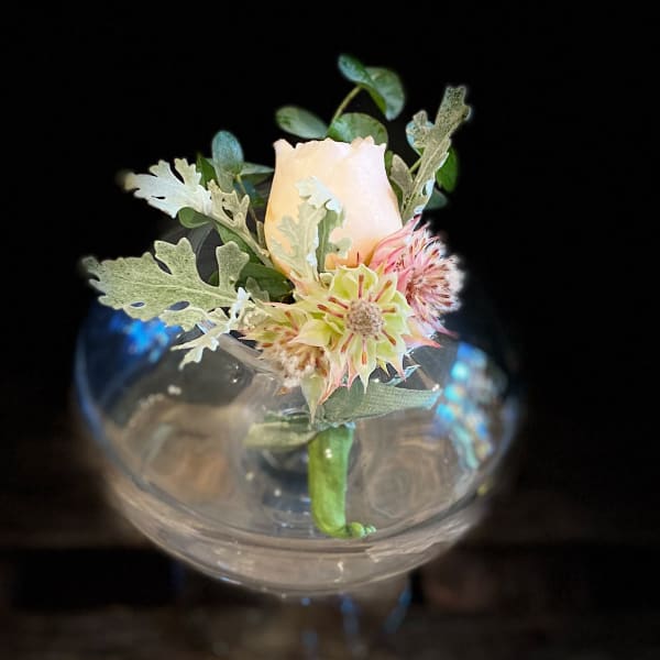 Single pale rose in a clear glass vase with small accent flowers