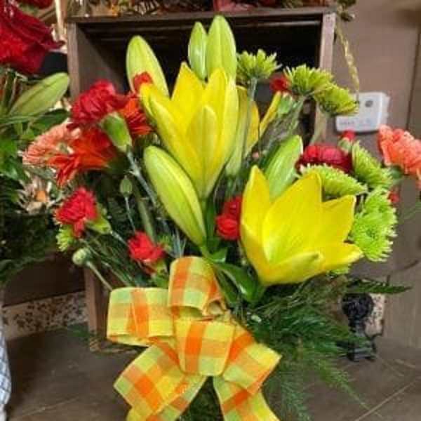 Bouquet of yellow lilies and red flowers in a glass vase with a plaid bow