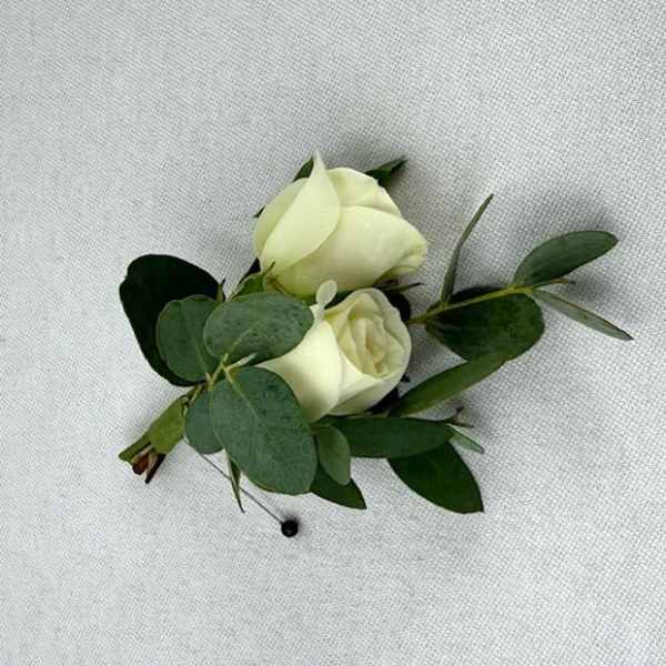 Two white rose buds with greenery on a fabric background