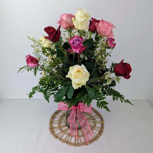 Bouquet of multicolored roses in a clear vase with a pink ribbon