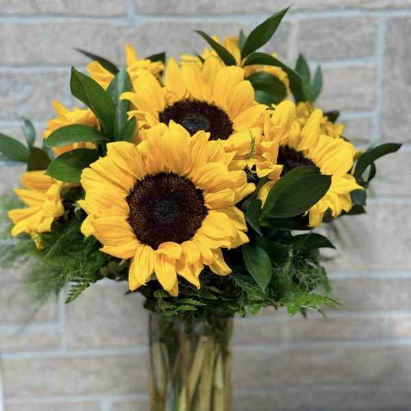 Tall glass vase of large yellow sunflowers with dark centers