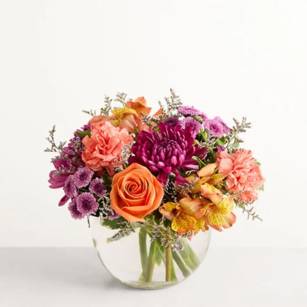 Mixed bouquet of orange, pink, and purple flowers in a clear glass vase