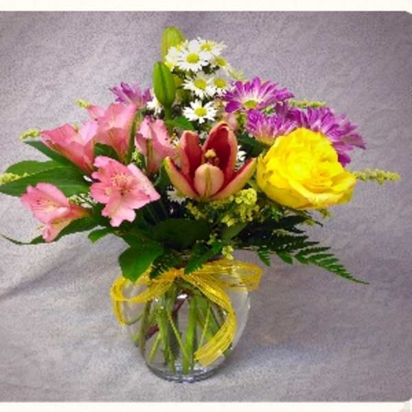 Mixed bouquet of pink, yellow, and purple flowers in a glass vase
