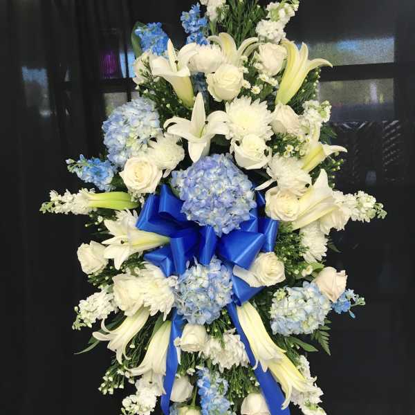 Standing floral spray with white lilies, roses, and blue hydrangeas on a black backdrop