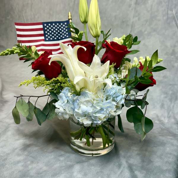 Red roses and white lilies in a glass vase with a small American flag